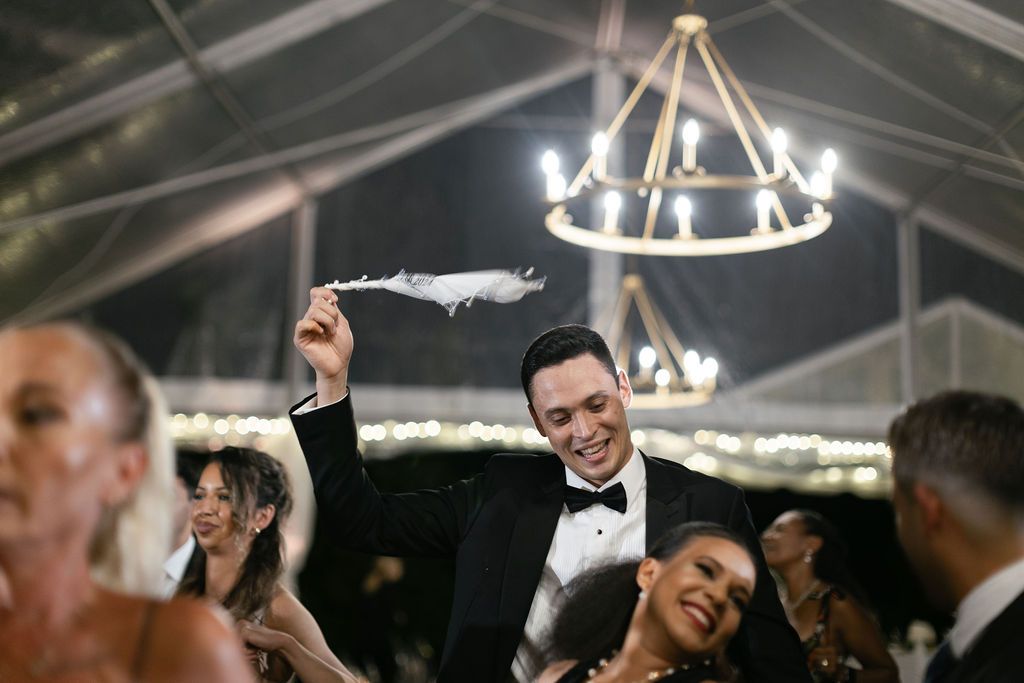 Lively celebration under a chandelier-lit tent with guests dancing and enjoying the festivities.