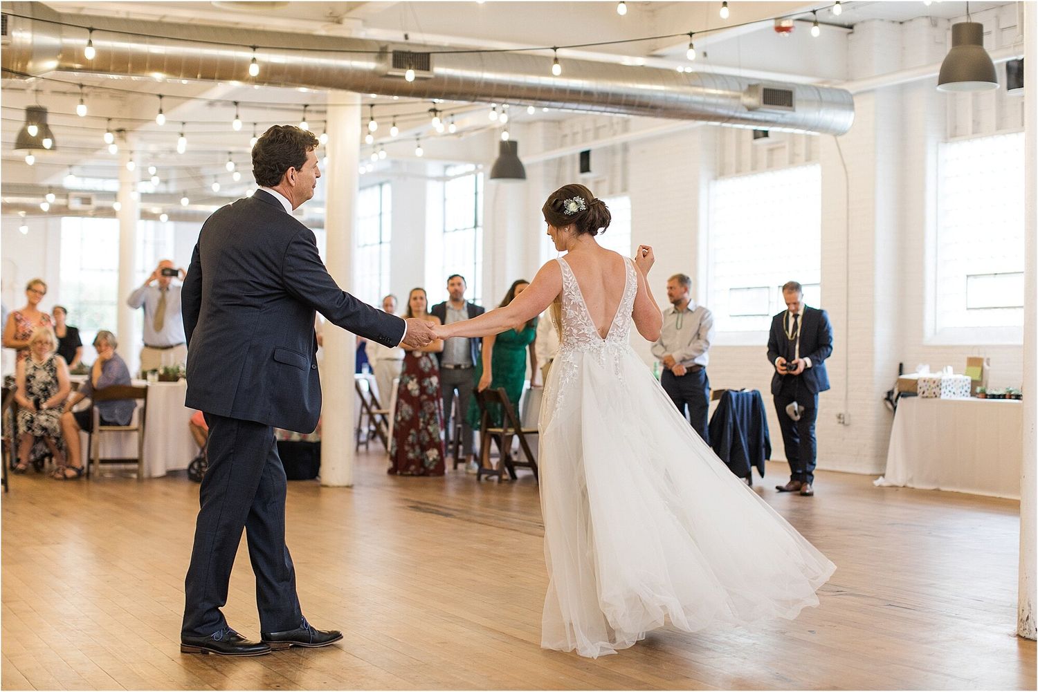 A couple dances in an open reception space with white columns and hardwood floors.