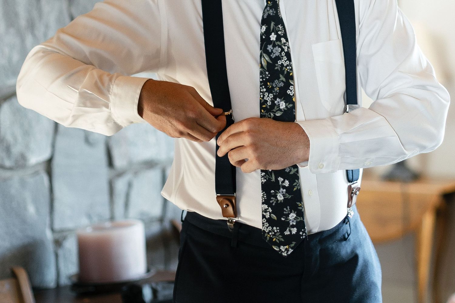 Close-up of person adjusting black suspenders and floral tie.