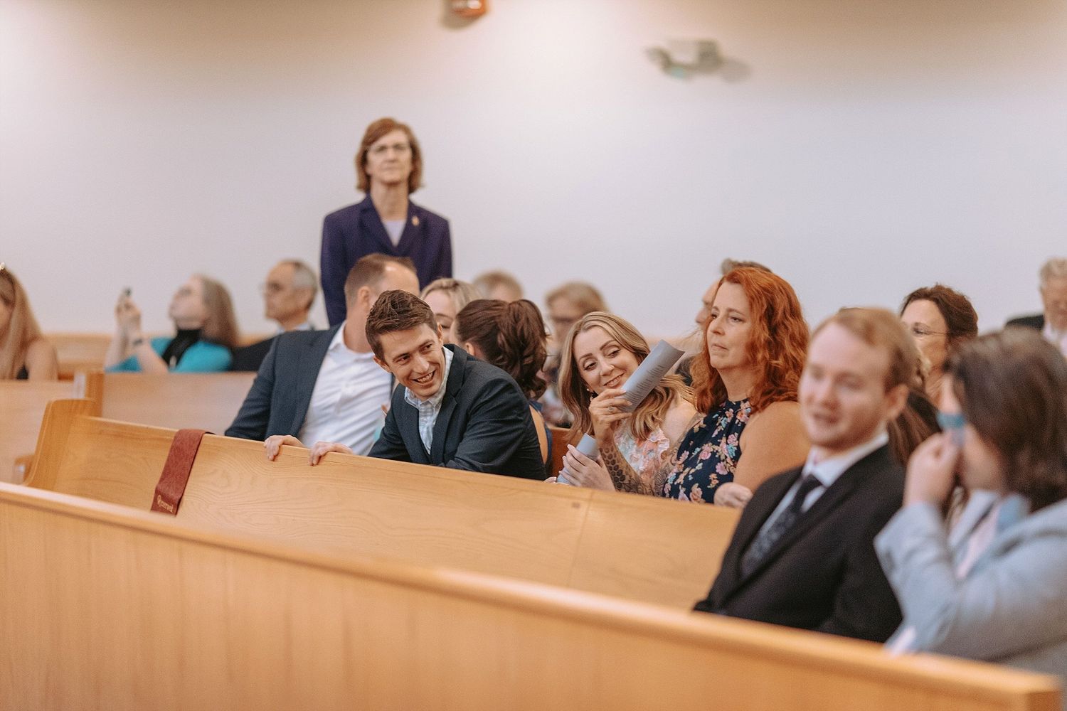 Wedding guests share joyful reactions while seated in wooden church pews during ceremony.