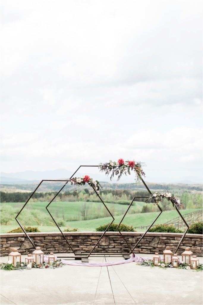 Modern geometric wedding arch with floral arrangements overlooking a scenic mountain landscape.