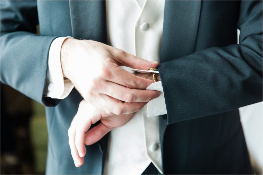 Close-up of formal attire with hands adjusting cufflinks and sleeves.