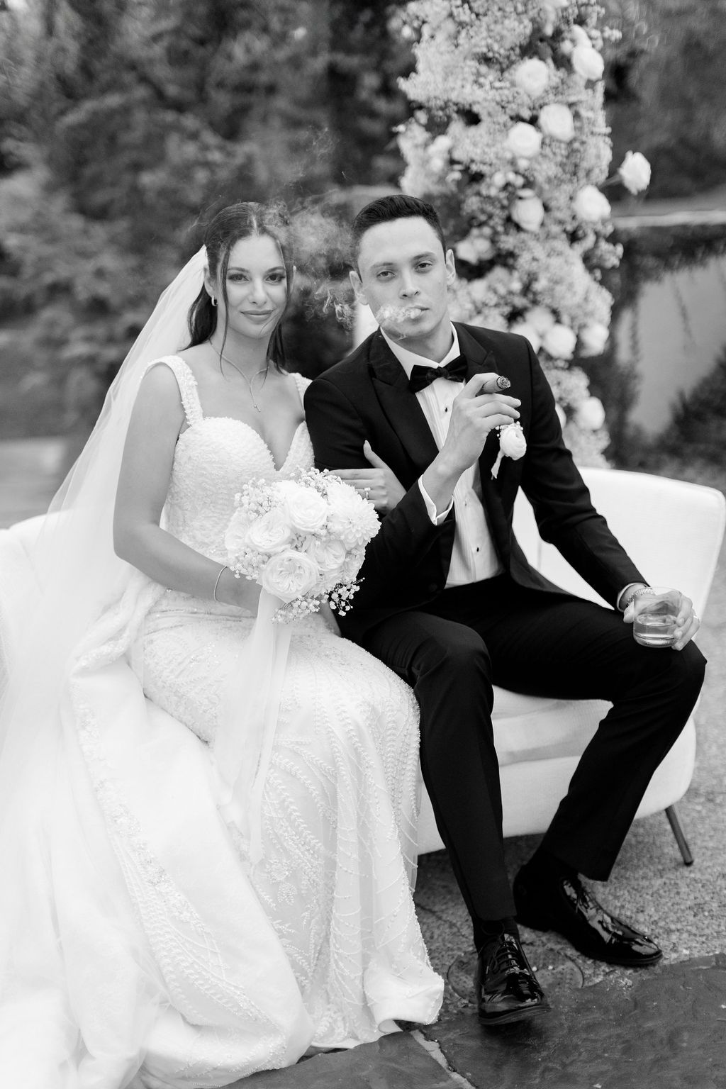 Black and white portrait of newlyweds seated together with elegant floral arrangements.