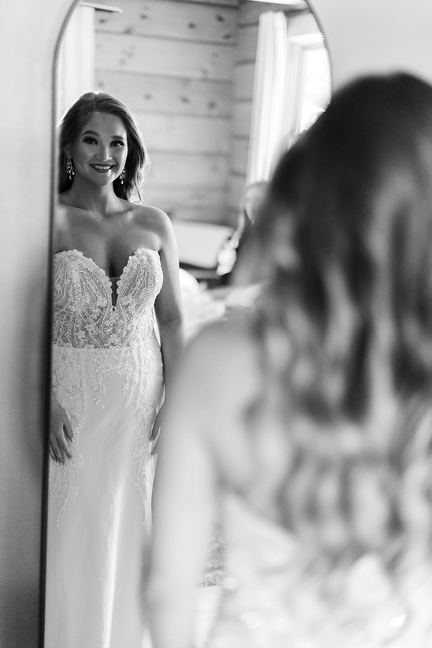 A bride admires her reflection in a mirror while wearing a stunning lace strapless wedding gown.