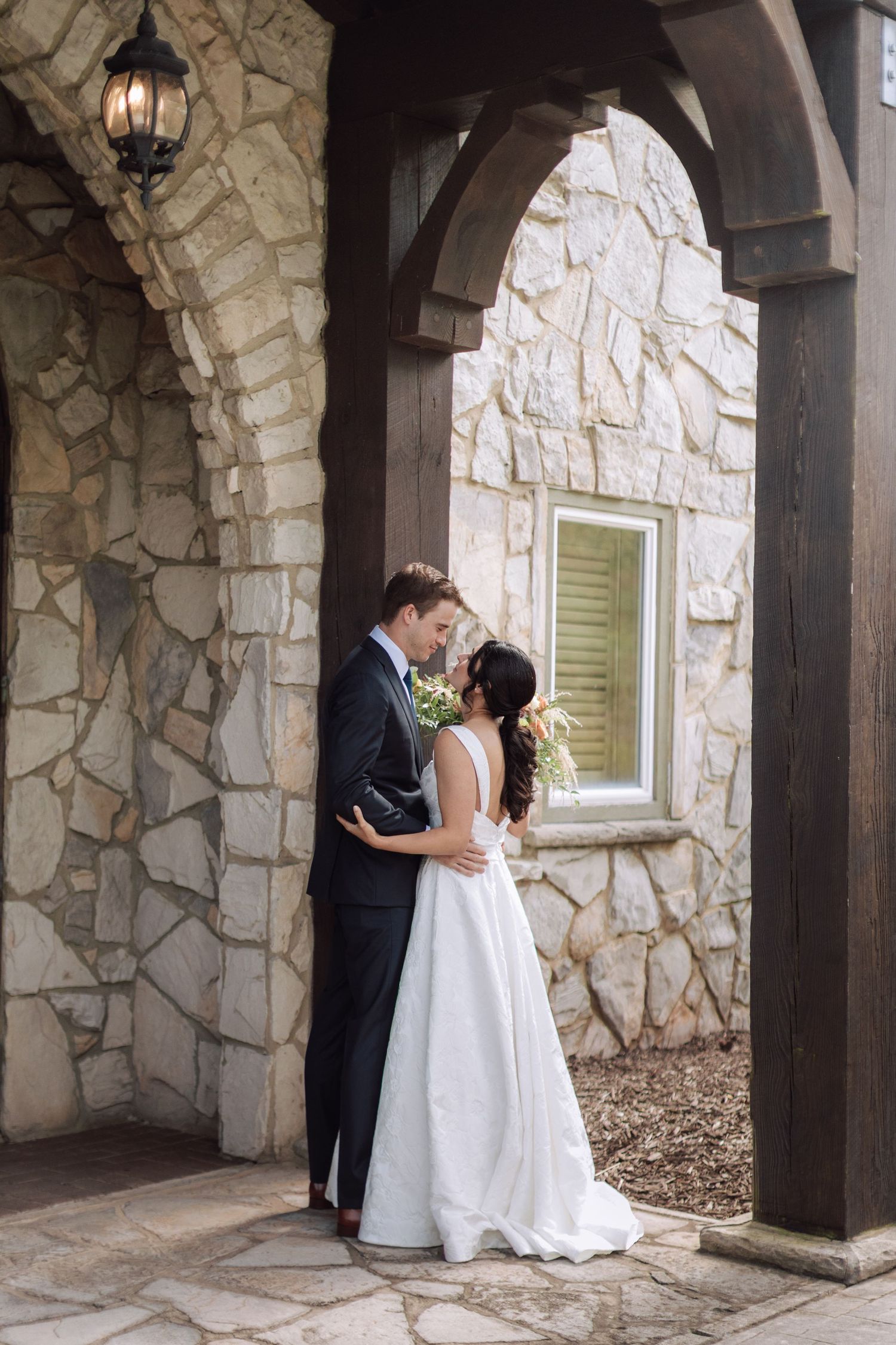 Bride and groom share romantic moment under stone arch at wedding venue.