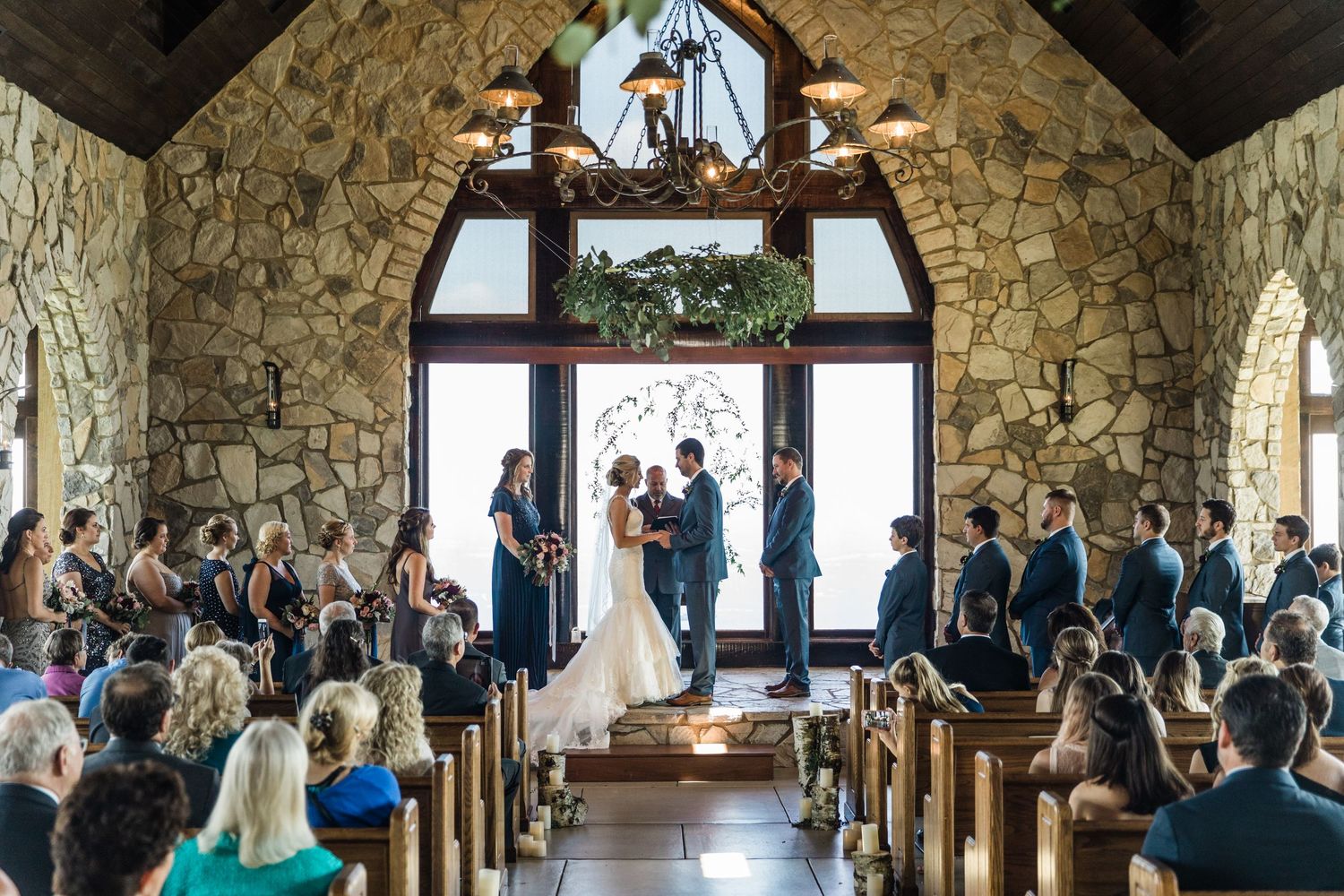 Wedding ceremony inside rustic stone Cliffs at Glassy chapel with exposed wooden beams and large windows.