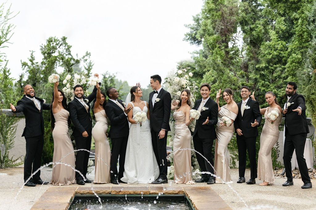 Wedding party poses together on stone patio with reflecting pool in foreground.