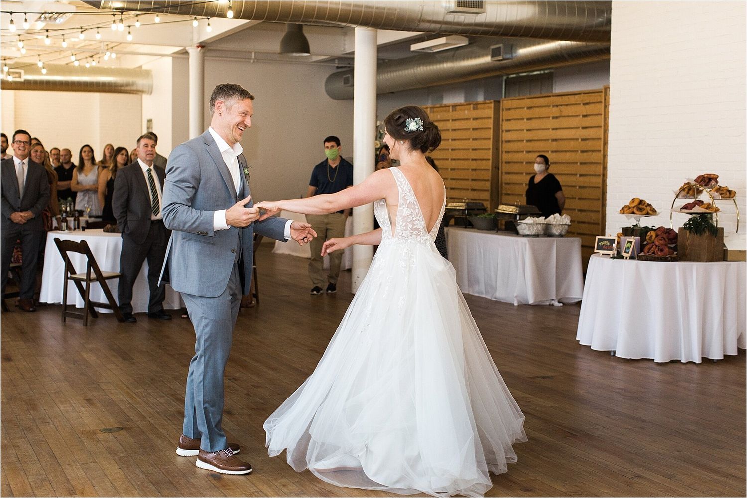 A couple shares their first dance in an elegant reception venue with hardwood floors and string lights.