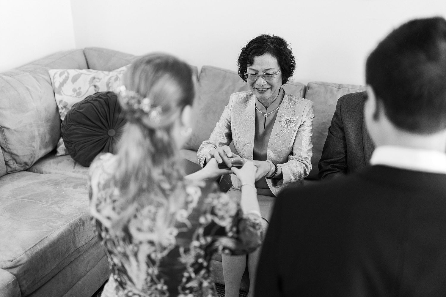 A black and white photo shows a casual indoor gathering with people sitting on a couch engaged in conversation.