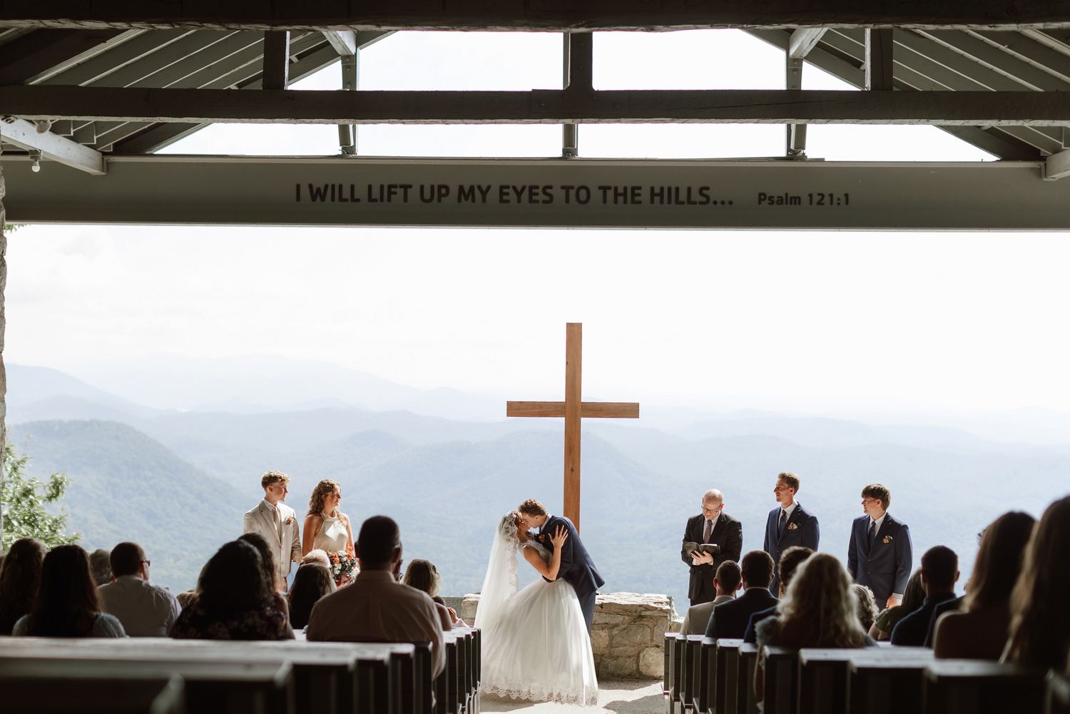 A couple exchanges vows at a mountaintop outdoor wedding chapel with a wooden cross.