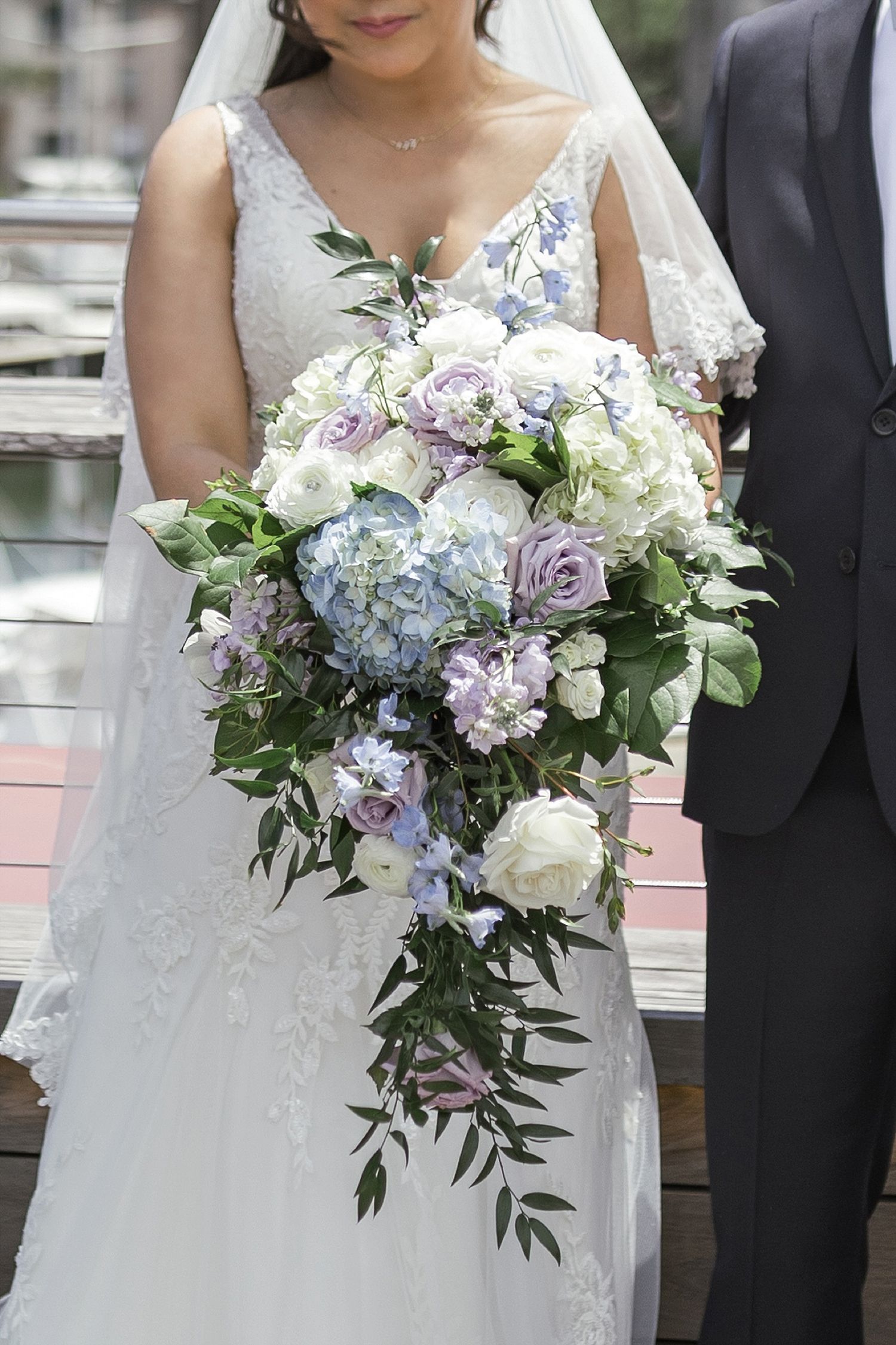 Close-up of cascading bridal bouquet with blue hydrangeas, purple roses, and trailing greenery.