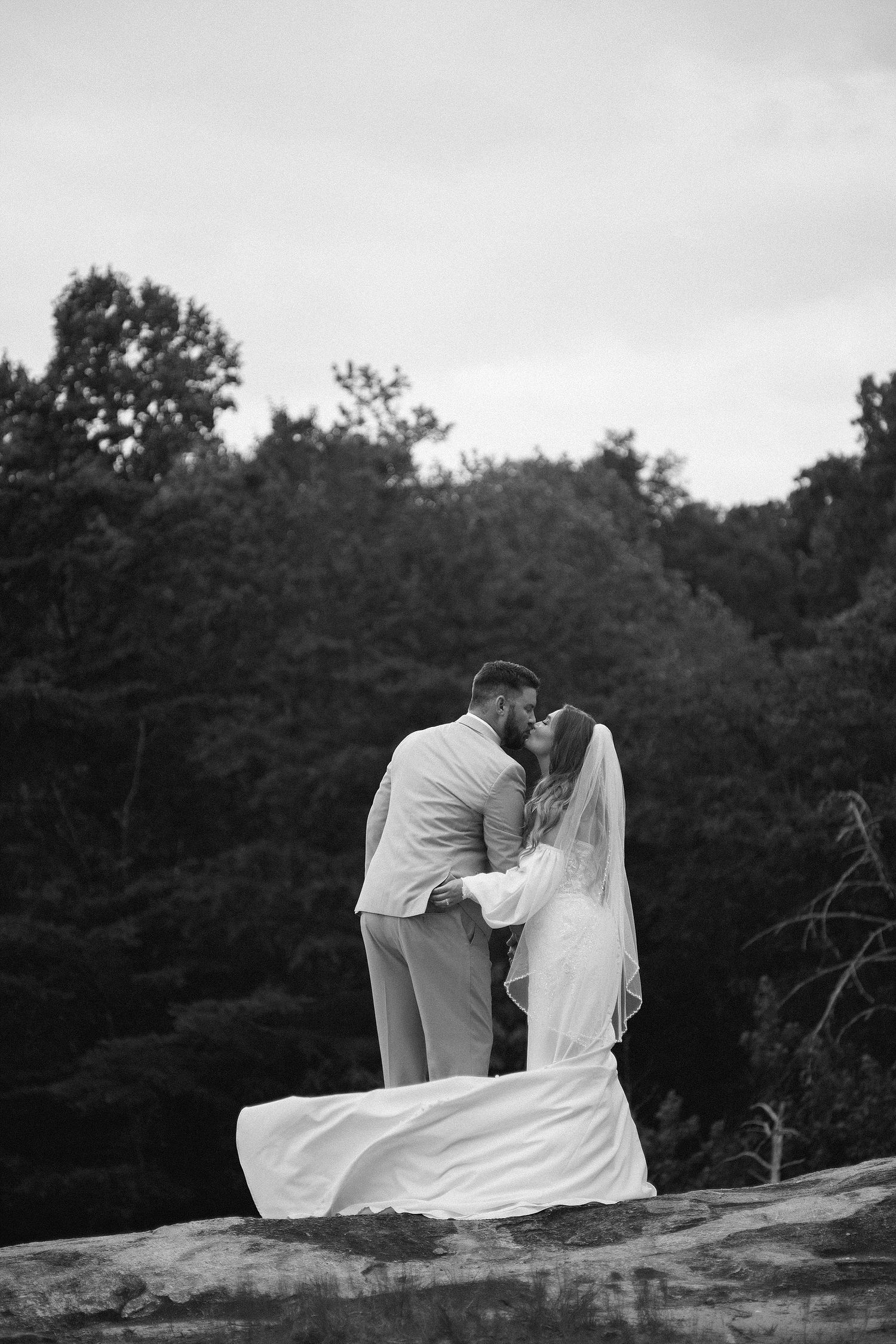 A romantic black and white portrait of newlyweds embracing on mountain outcrop.