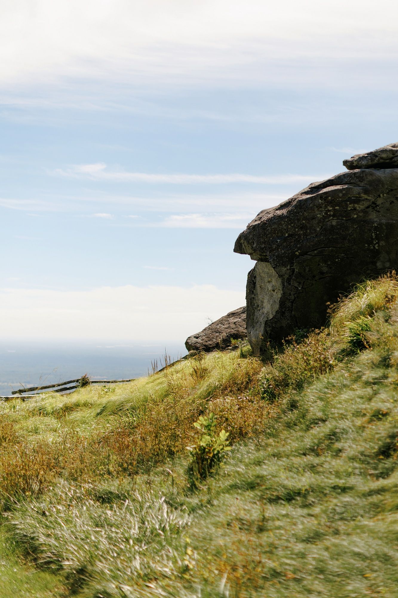 Rolling grassy hillside with dark rocky outcrops against cloudy sky at coastal viewpoint.