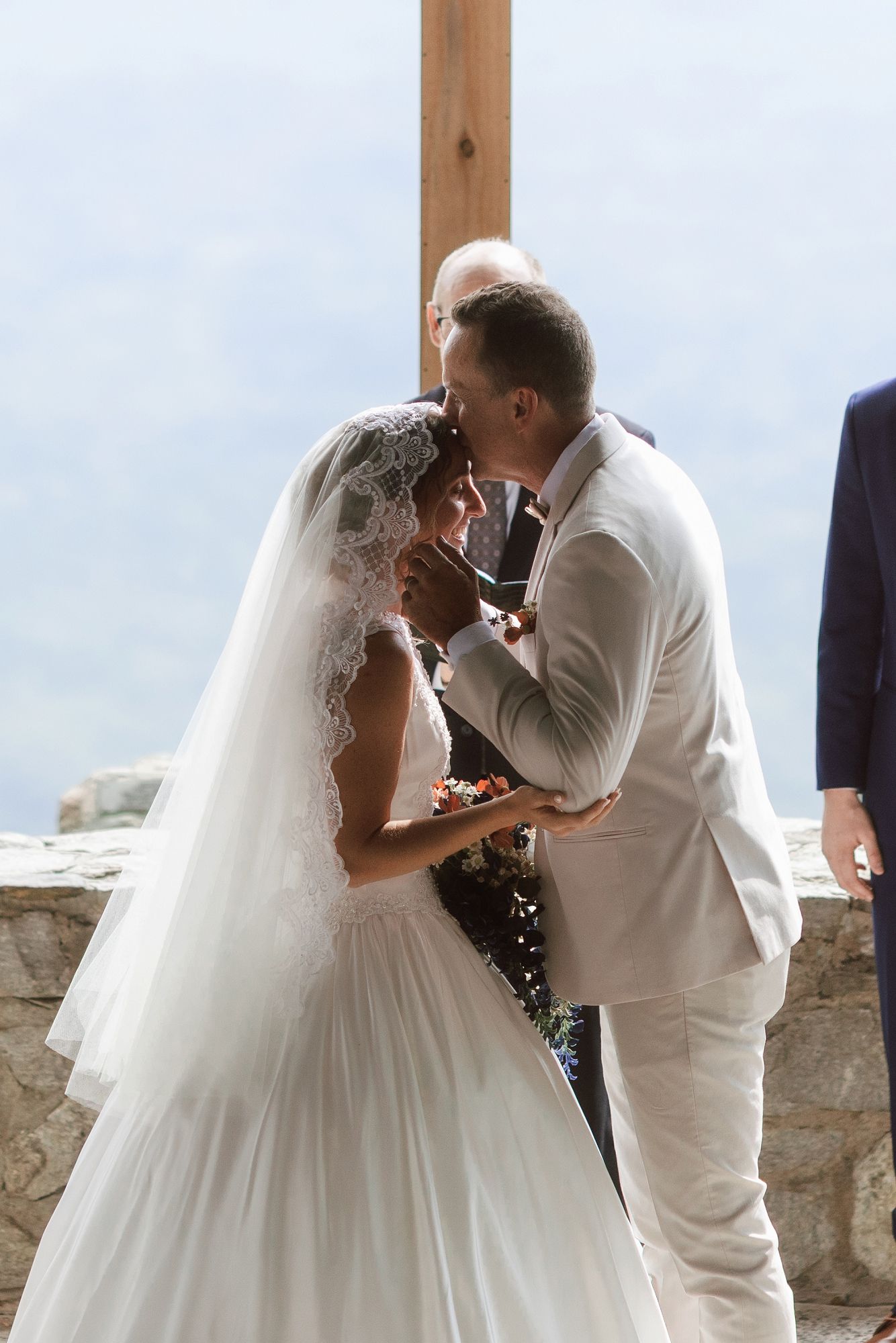 Bride and groom share their first kiss at an outdoor wedding ceremony with a wooden cross backdrop.
