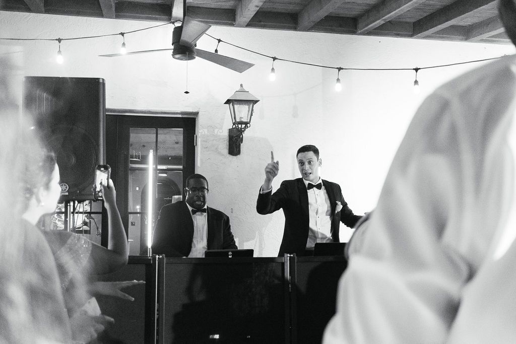 A black and white image of people celebrating at an indoor reception with hanging lights.