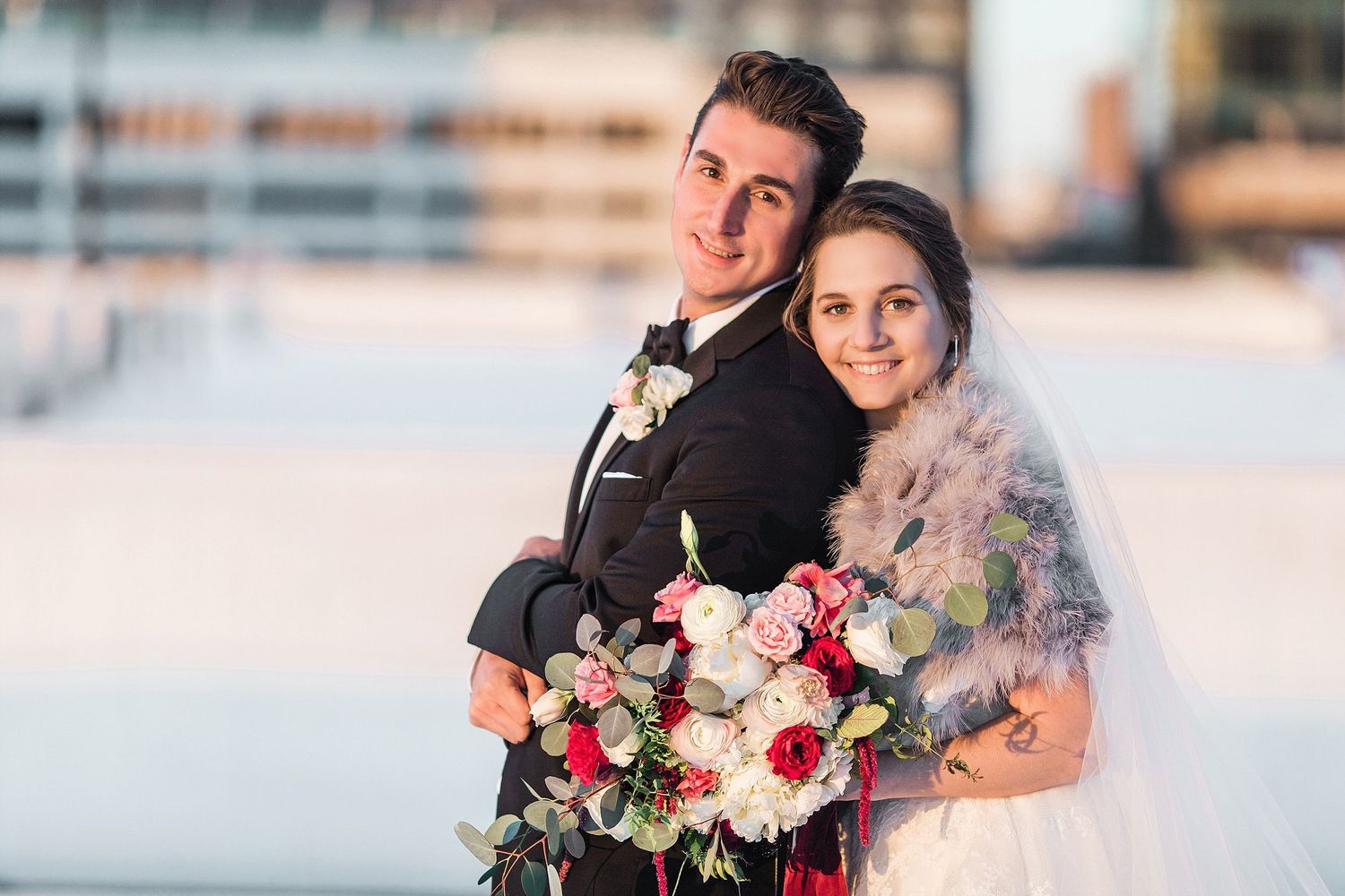 Romantic sunset wedding portrait with couple holding pink and red bouquet.