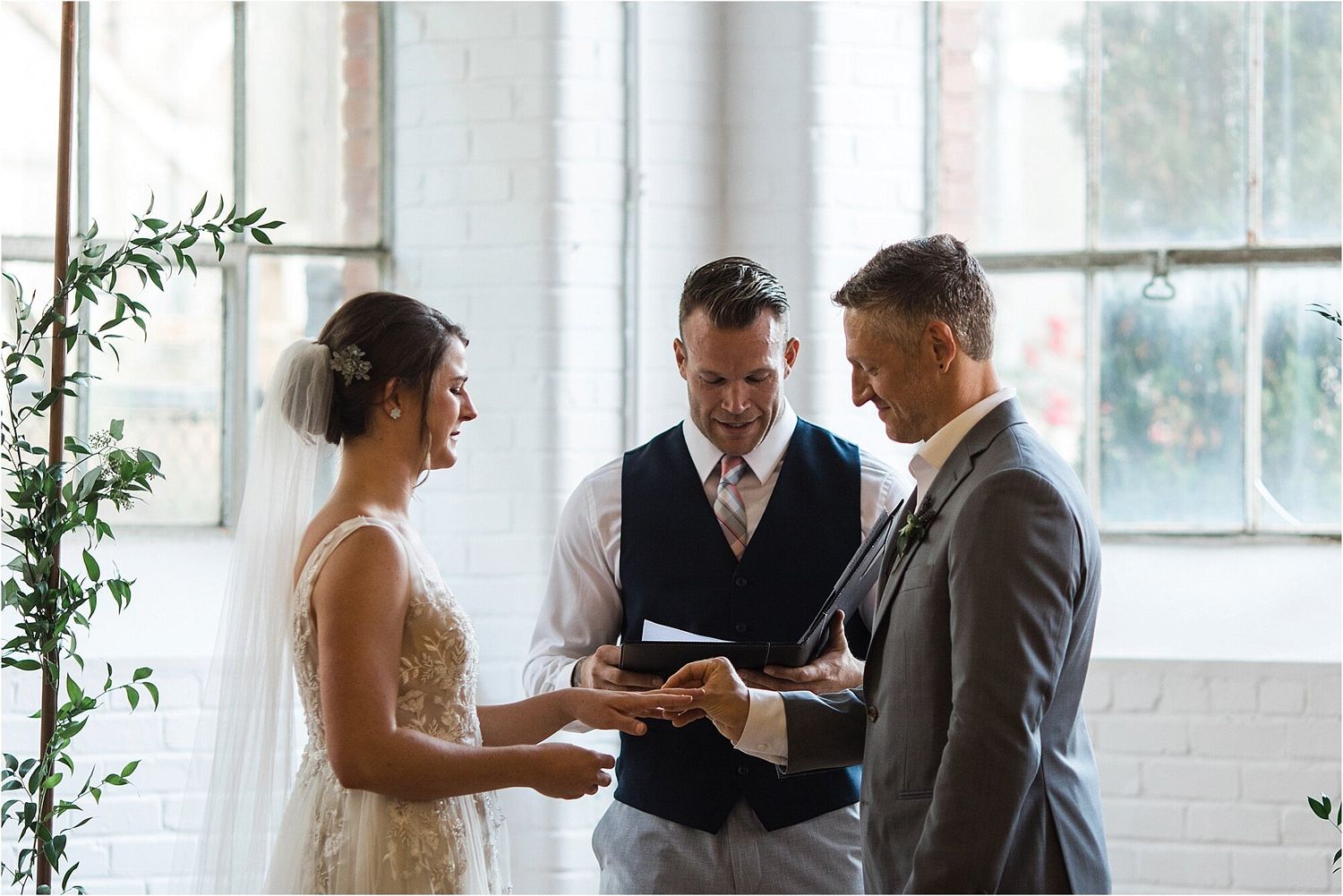 An intimate wedding ceremony moment captured in a light-filled room with white brick walls.