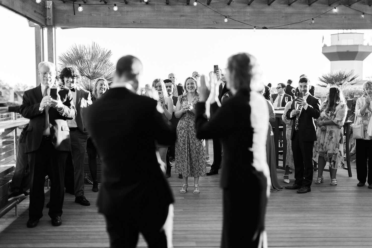 Silhouettes of wedding guests dancing at an outdoor reception under covered patio.