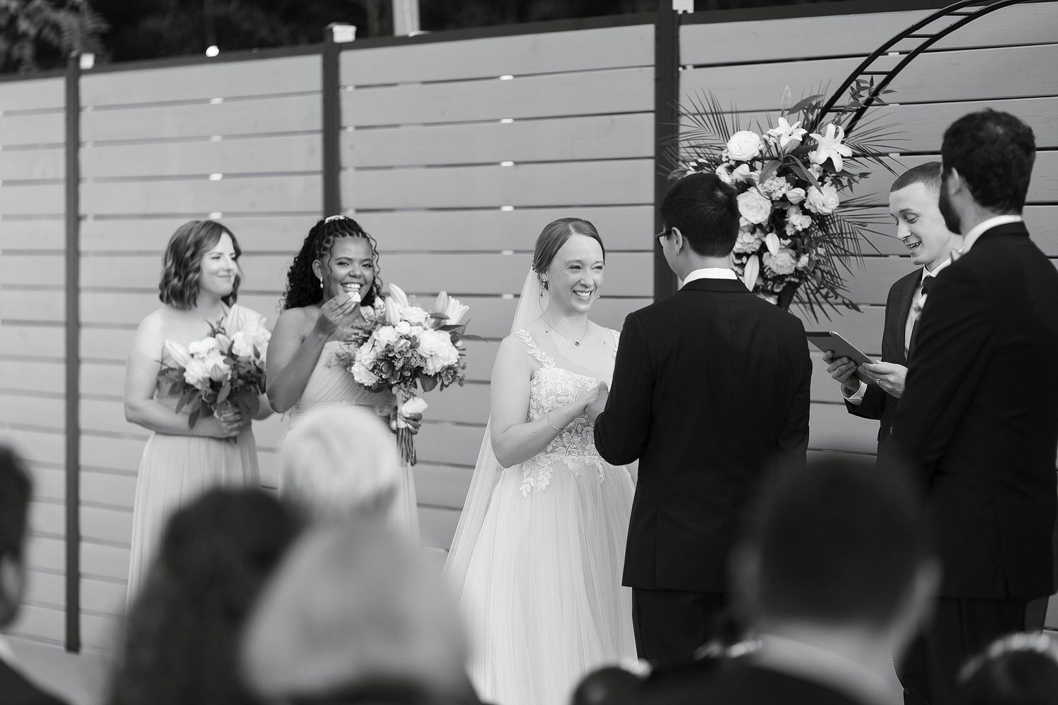 Black and white photo of an intimate outdoor wedding ceremony with bridesmaids holding bouquets beside the married couple.