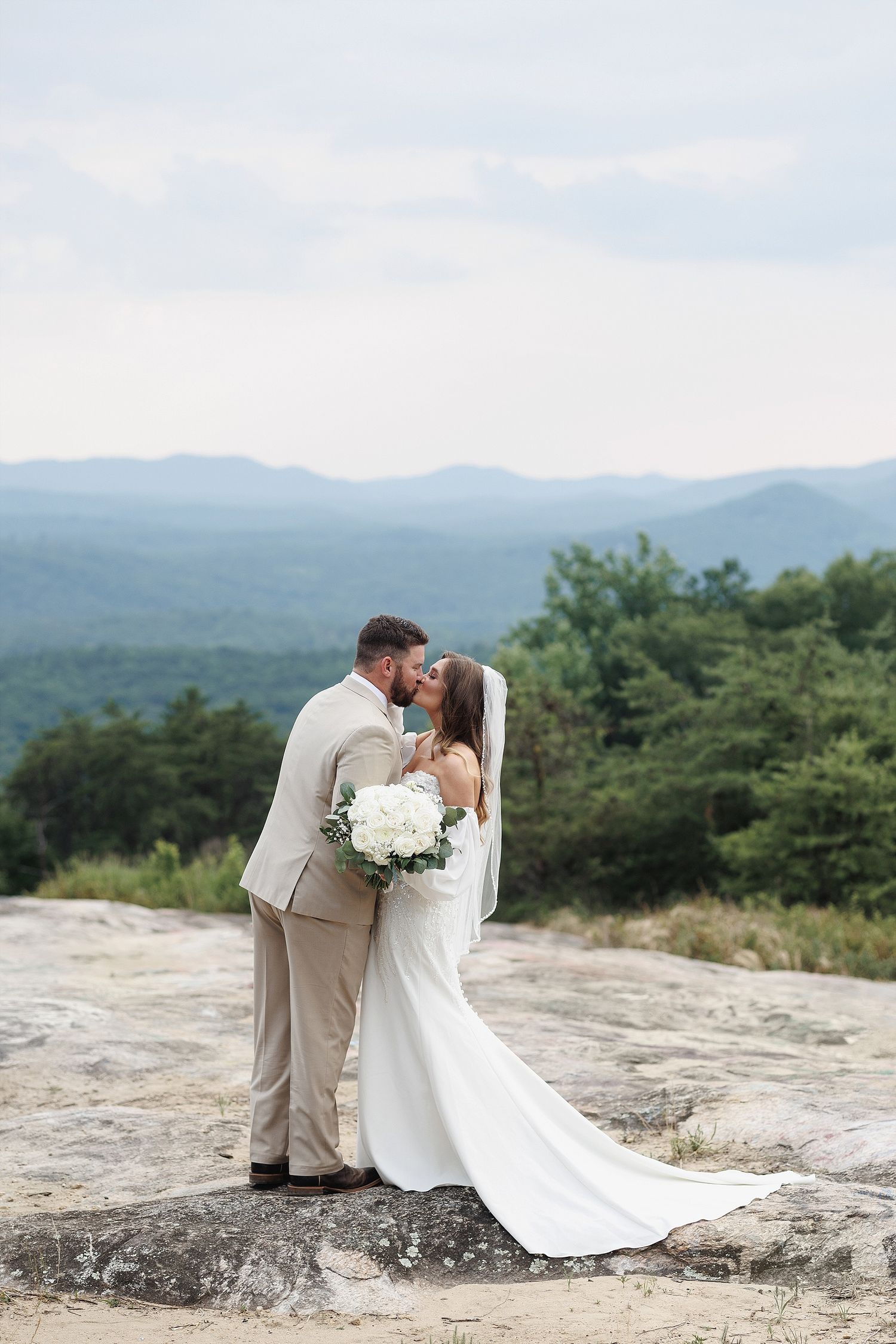 Wedding couple shares romantic moment on rocky mountain overlook with flowing white dress.
