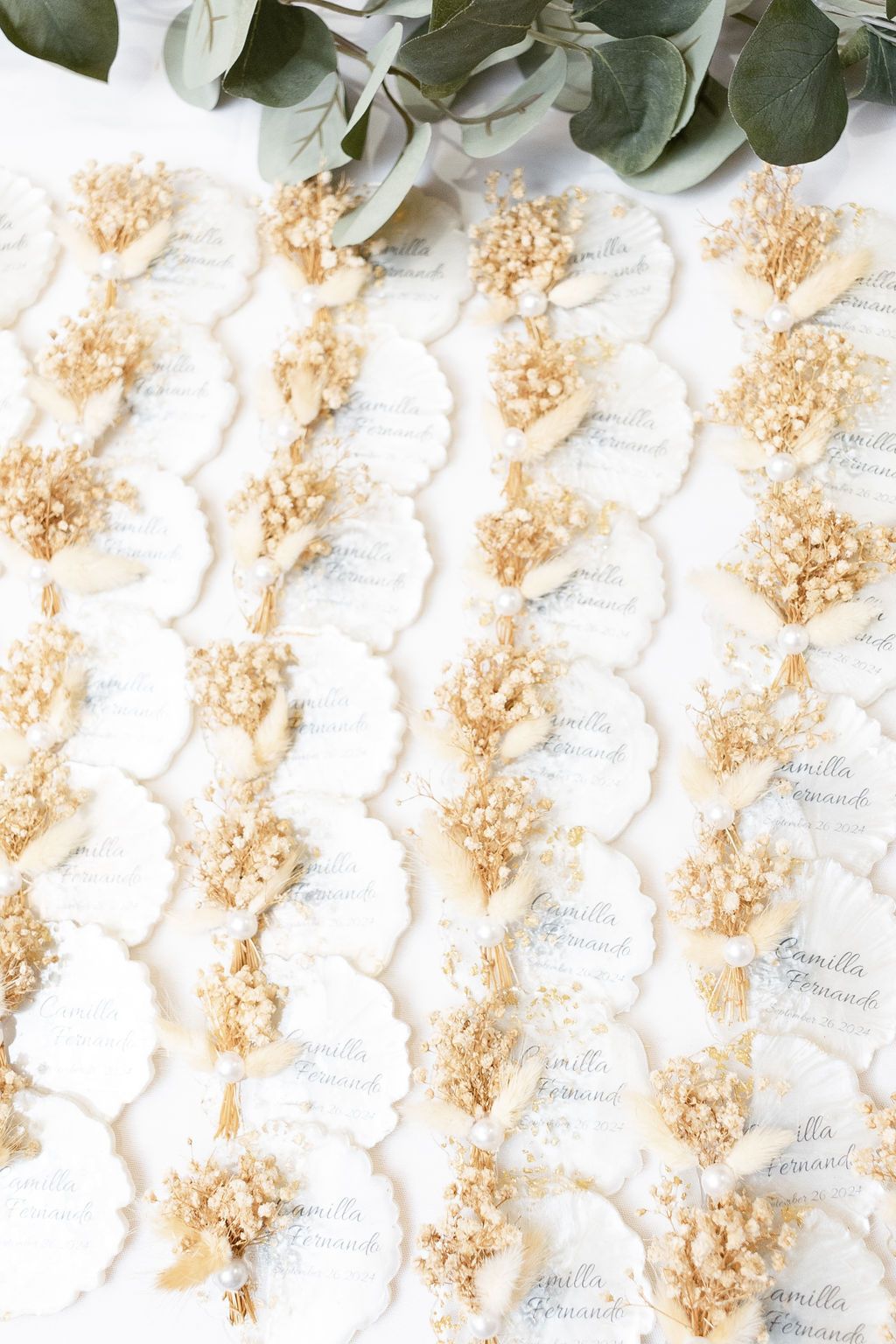 Wedding place cards arranged in rows with dried baby's breath flowers and eucalyptus leaves on white background.