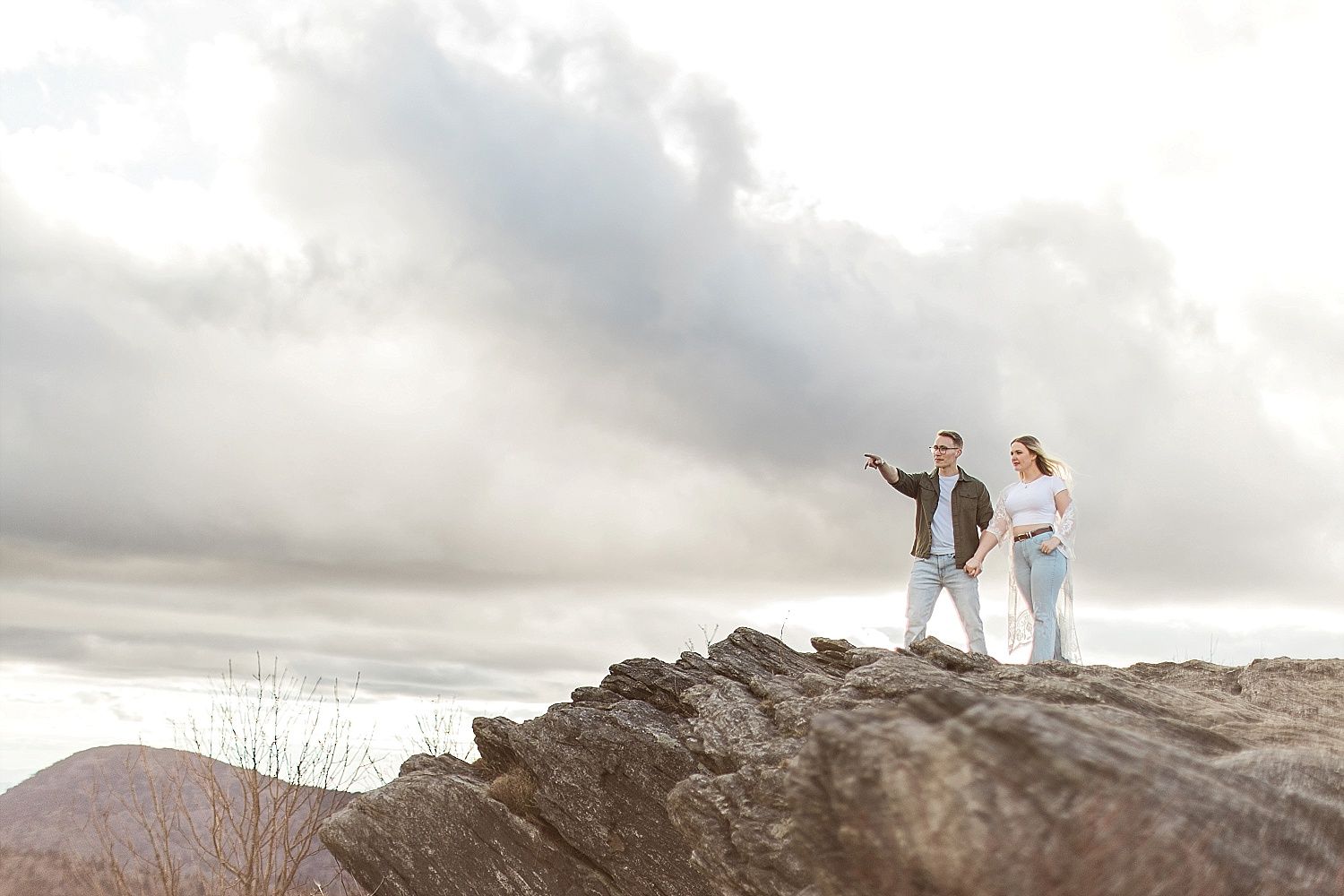 A couple stands on a mountaintop during their engagement pictures under epic skies