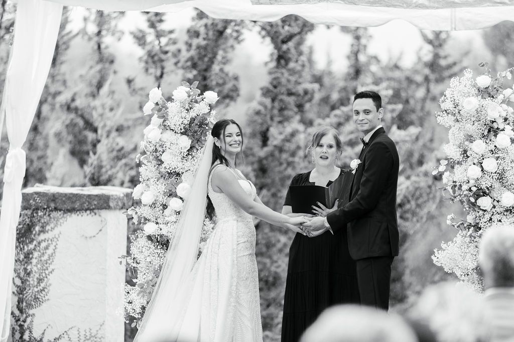 Black and white wedding ceremony photo with floral arch decorations.