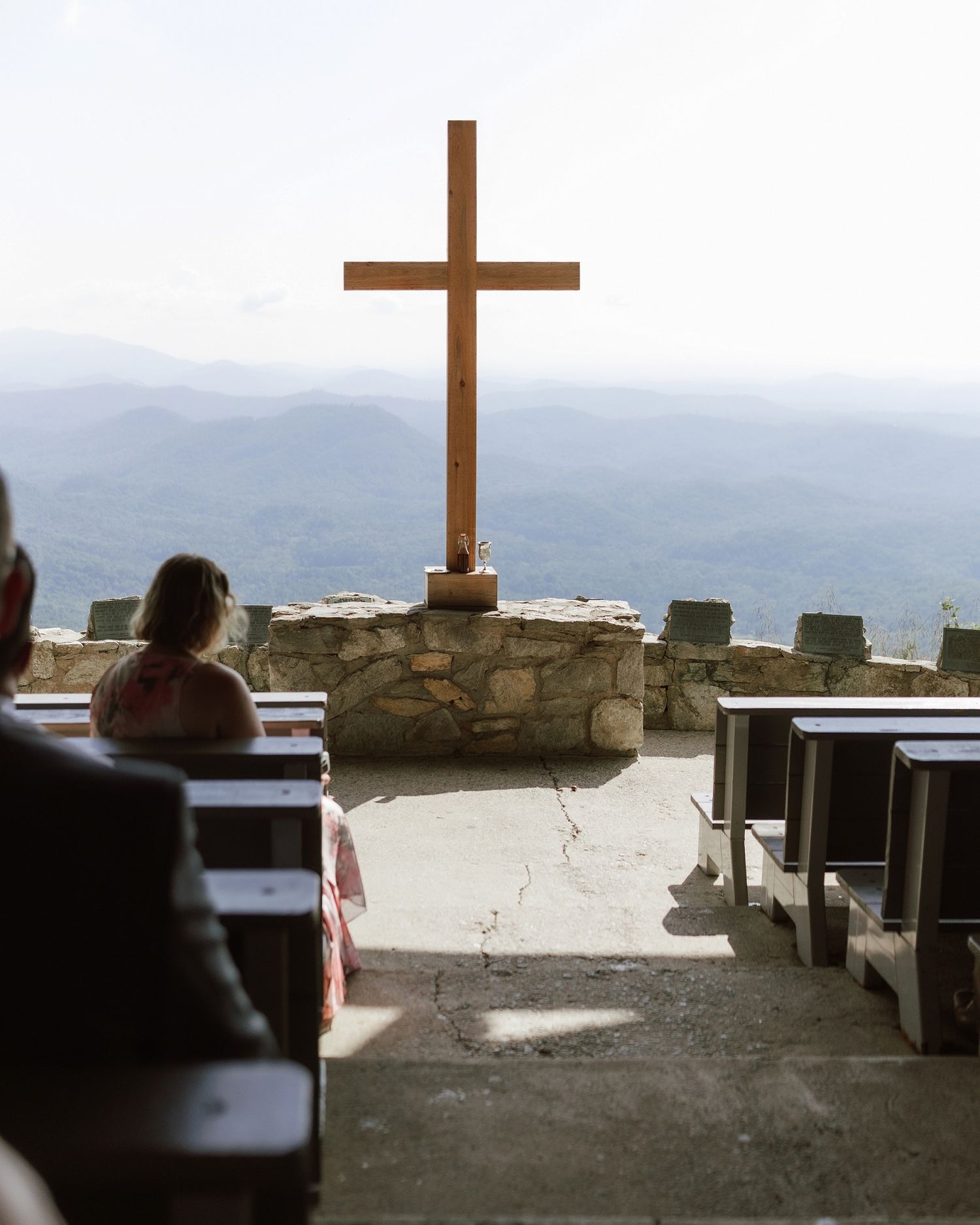 Open-air mountain chapel with wooden cross, stone altar, and scenic misty mountain views during an outdoor wedding ceremony.