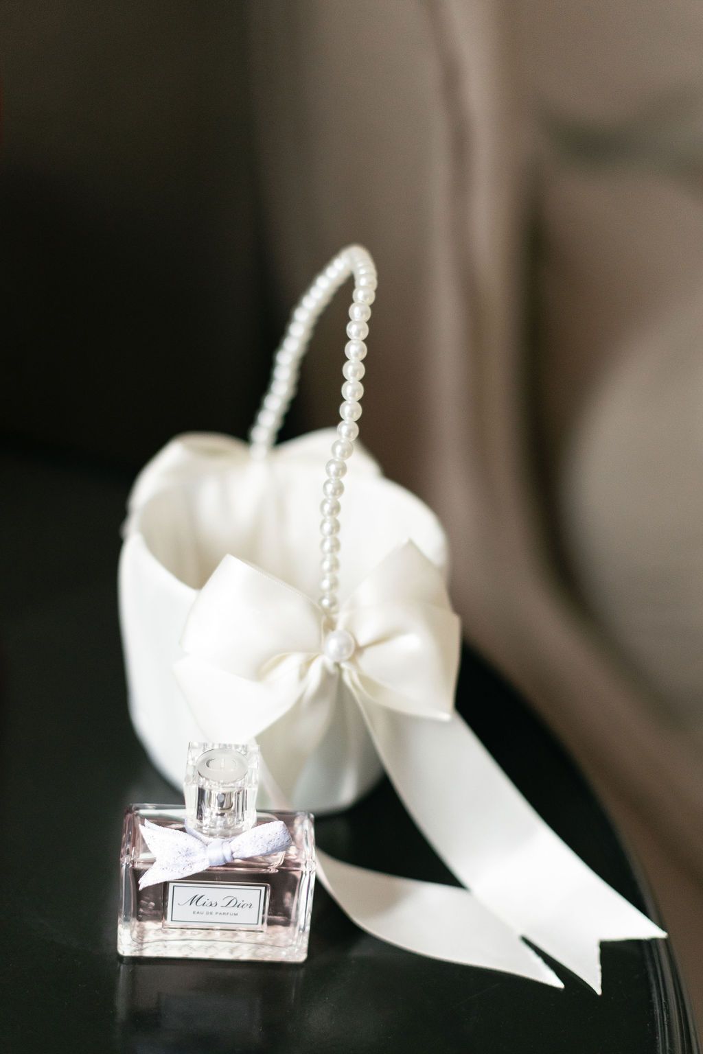 Elegant perfume bottle with white bow and pearl handle displayed on dark surface.