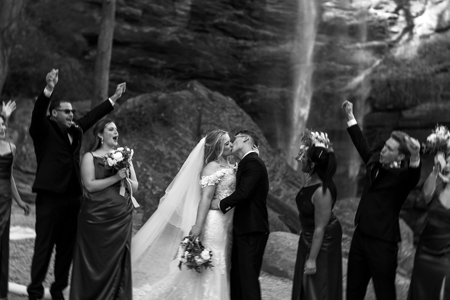 Black and white wedding photo showing ceremony moment inside canyon with waterfall and guests celebrating.