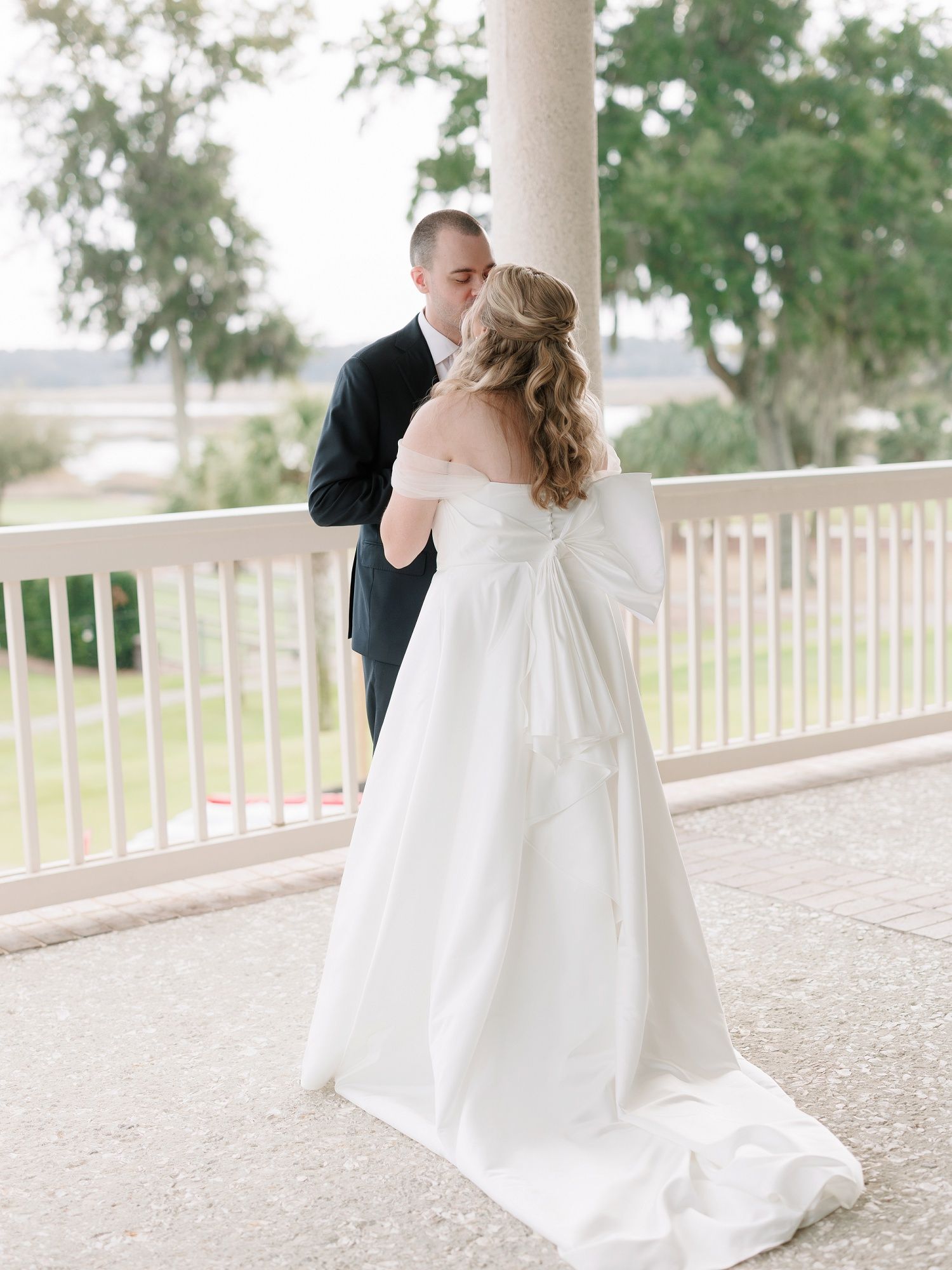 Wedding couple sharing intimate moments on a white columned porch with greenery in background.