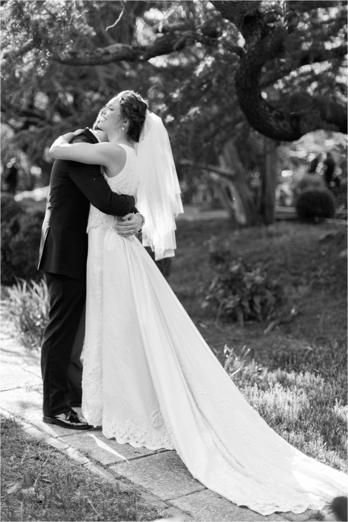 Black and white portrait of embracing newlyweds with long flowing wedding dress train.