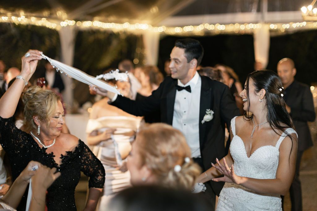 Wedding reception guests dancing and celebrating under a tent with twinkling lights.