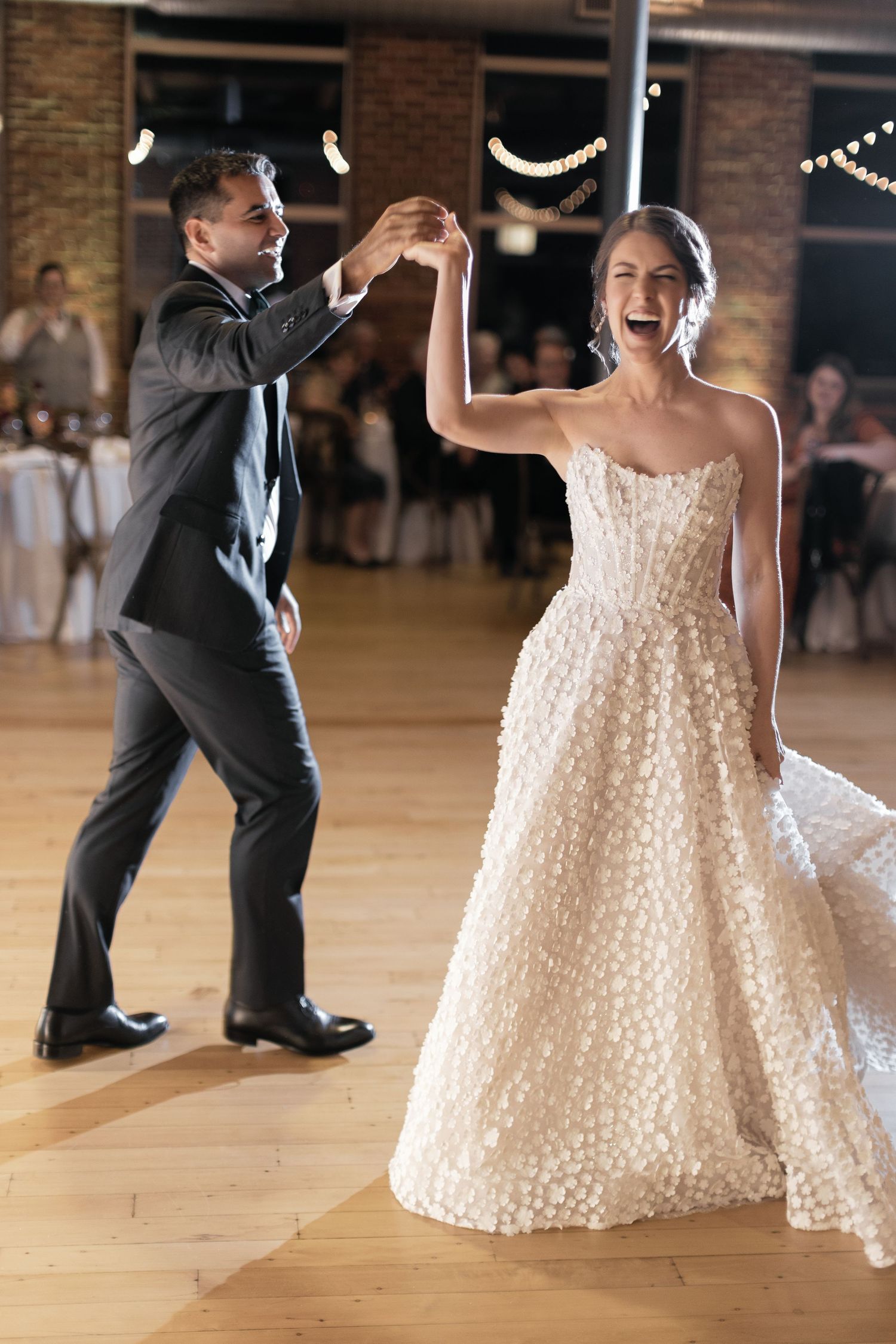 Bride and groom share joyful first dance, bride twirling in floral ballgown at elegant wedding reception.