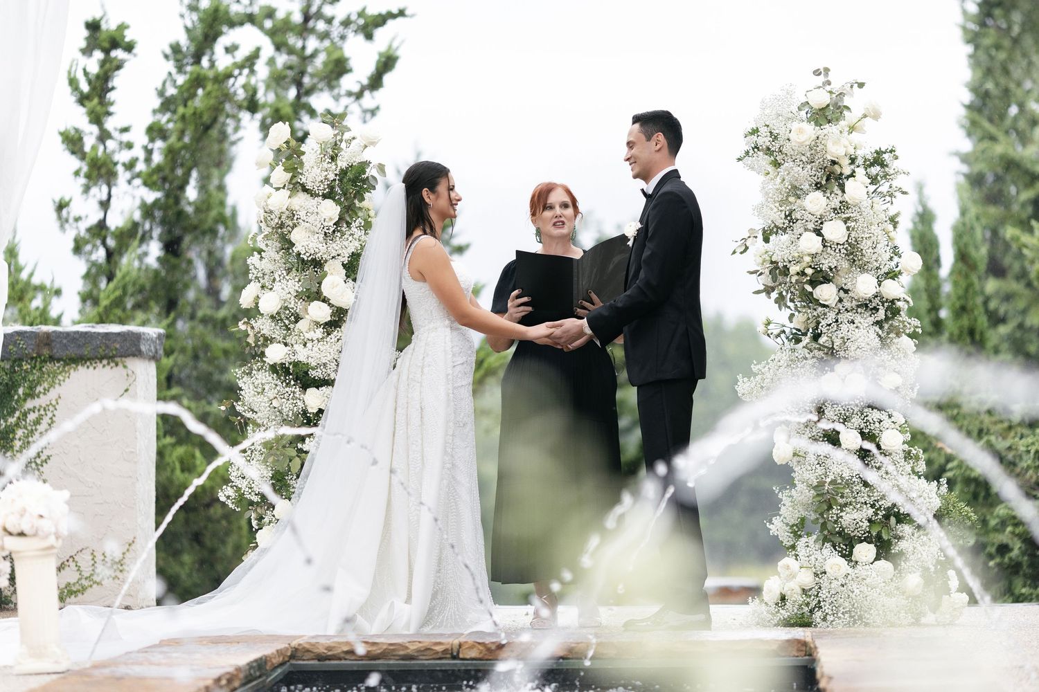 Outdoor wedding ceremony with floral arrangements and elegantly dressed couple at altar with officiant.
