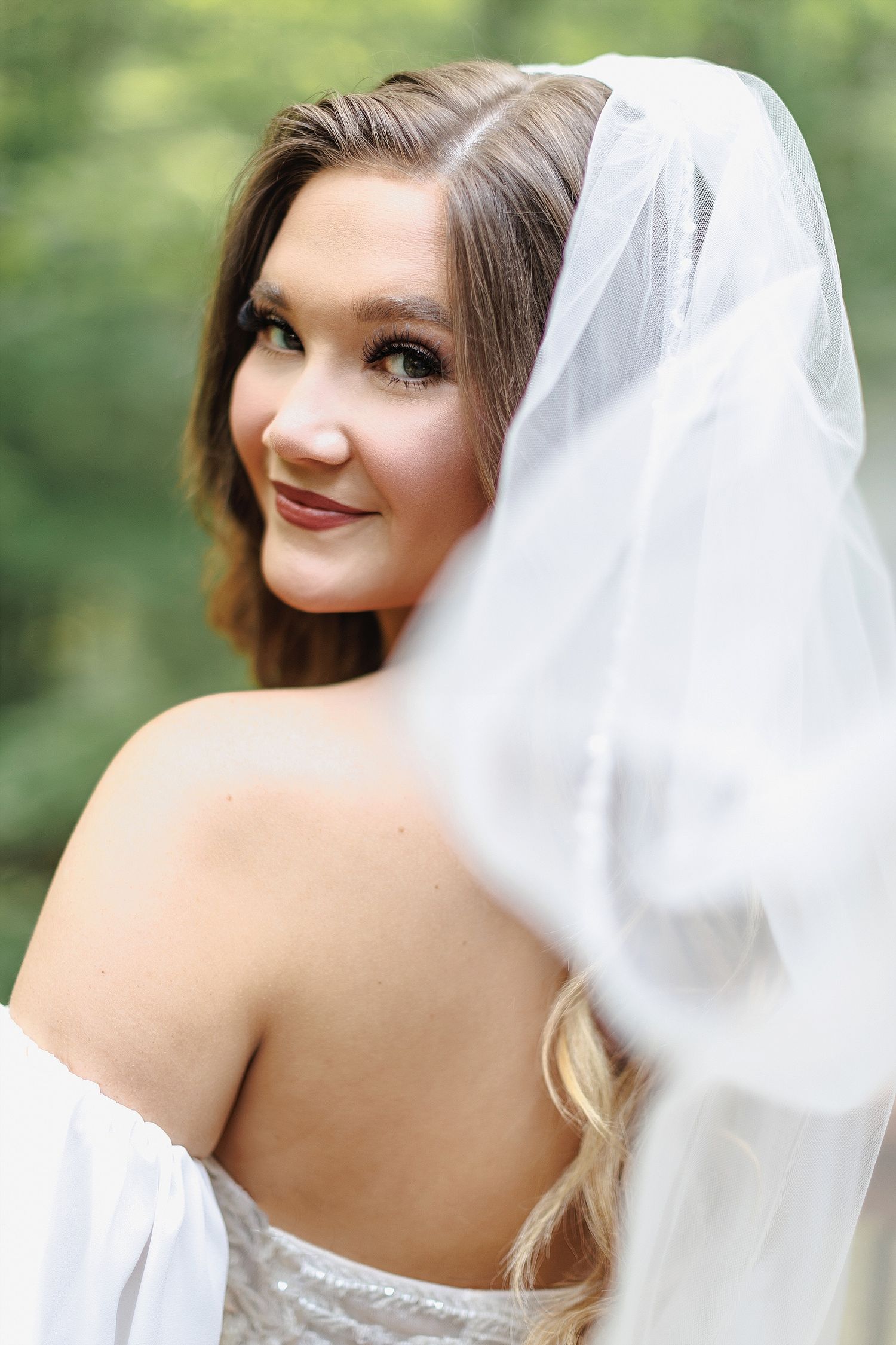 Elegant bridal portrait with flowing veil against natural forest background.