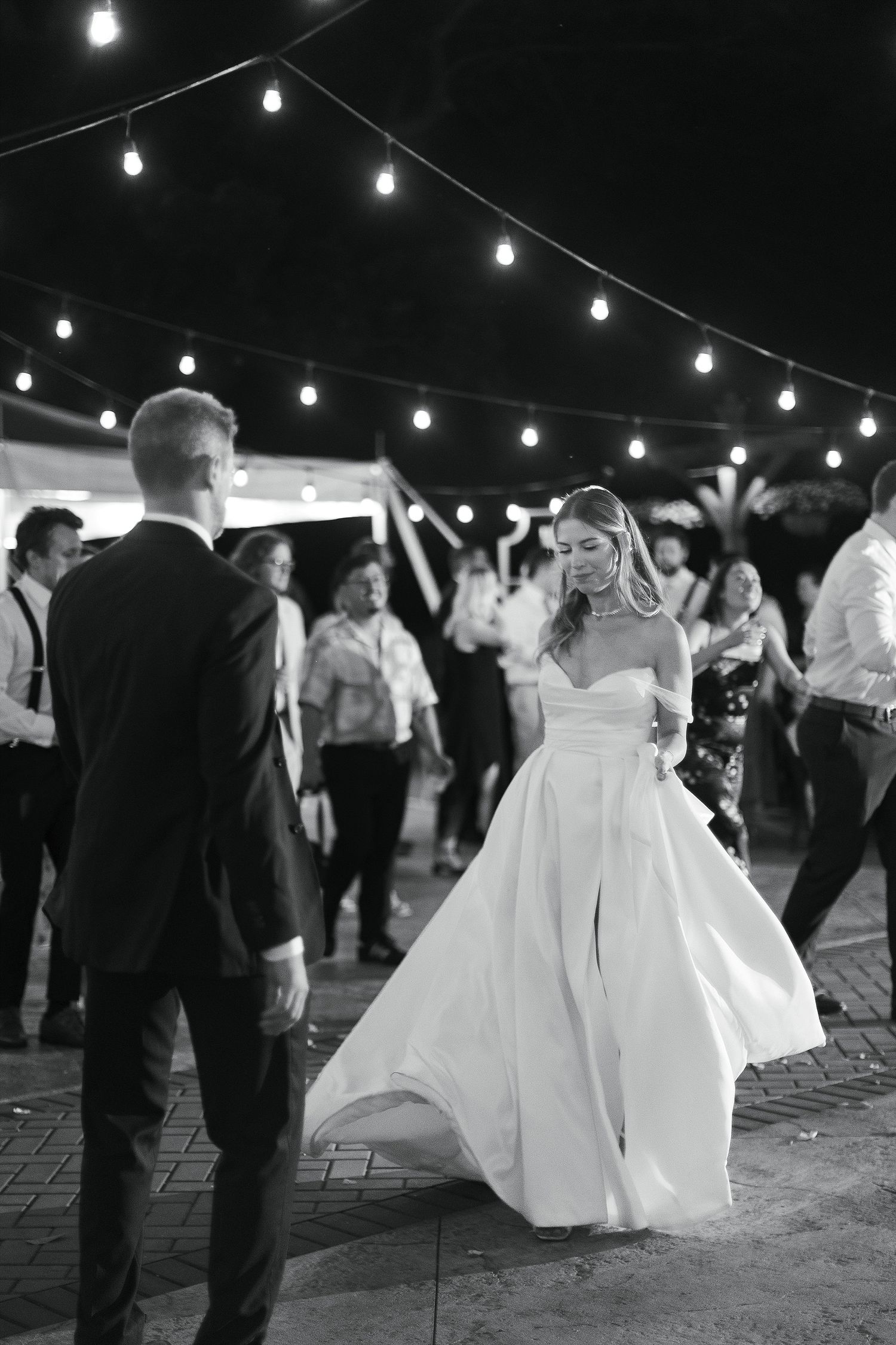 A couple dances beneath string lights at an outdoor wedding reception venue.