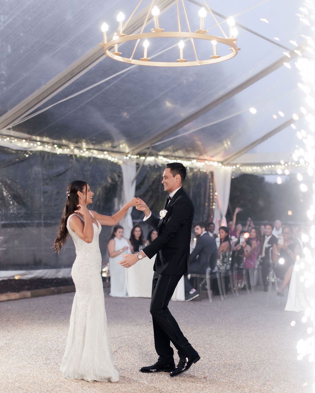 Couple sharing a playful dance under string lights in clear tent reception space.