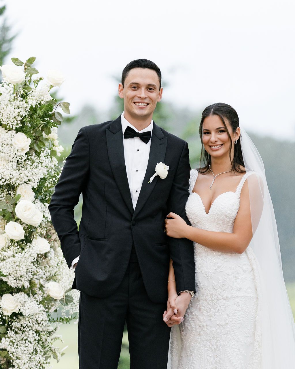 An elegant wedding portrait featuring a couple standing by white floral arrangements outdoors.