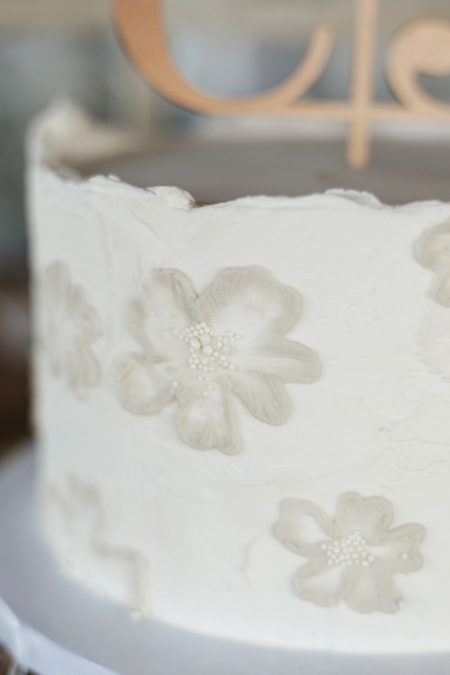 Close-up detail of a white wedding cake decorated with delicate gray floral patterns and beaded centers.