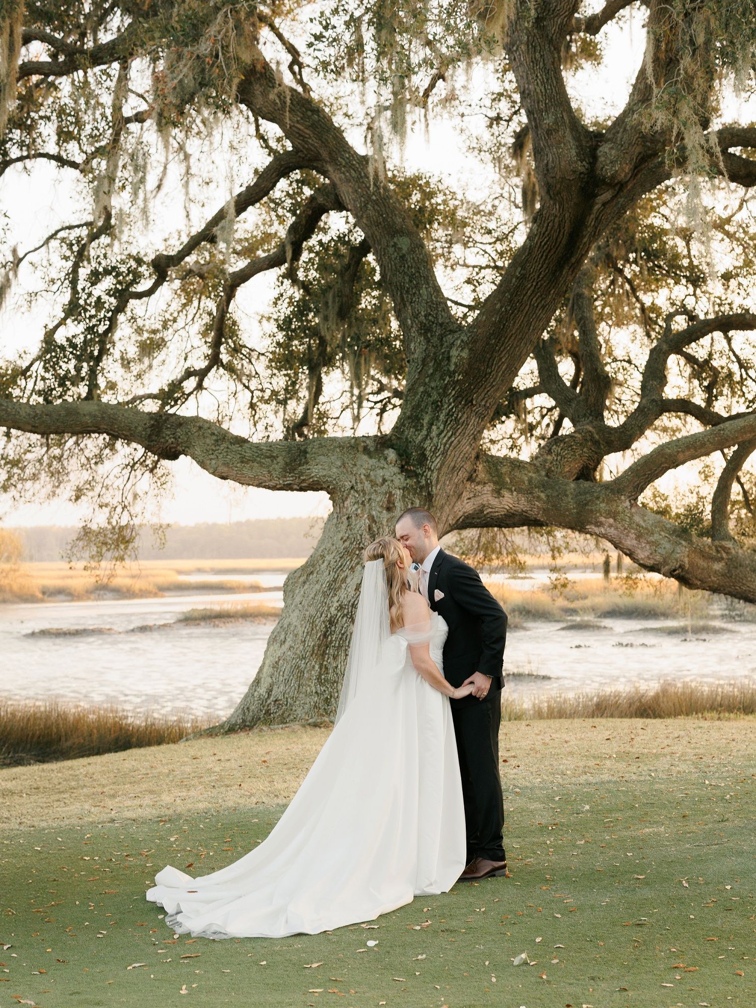 Wedding couple poses for romantic portraits under majestic oak trees at sunset.