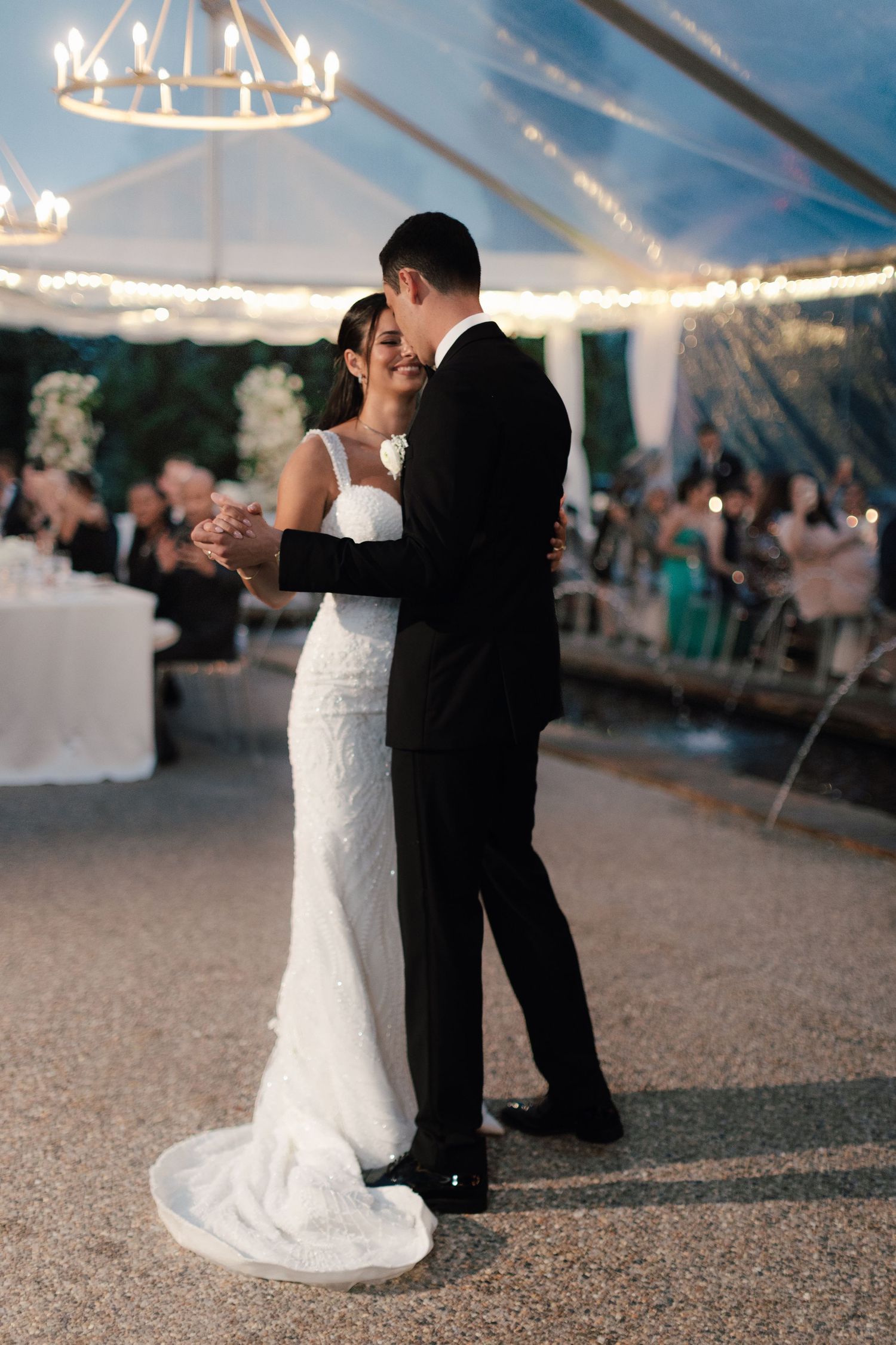 Bride and groom share their first dance under a chandelier in an elegant tented wedding reception.