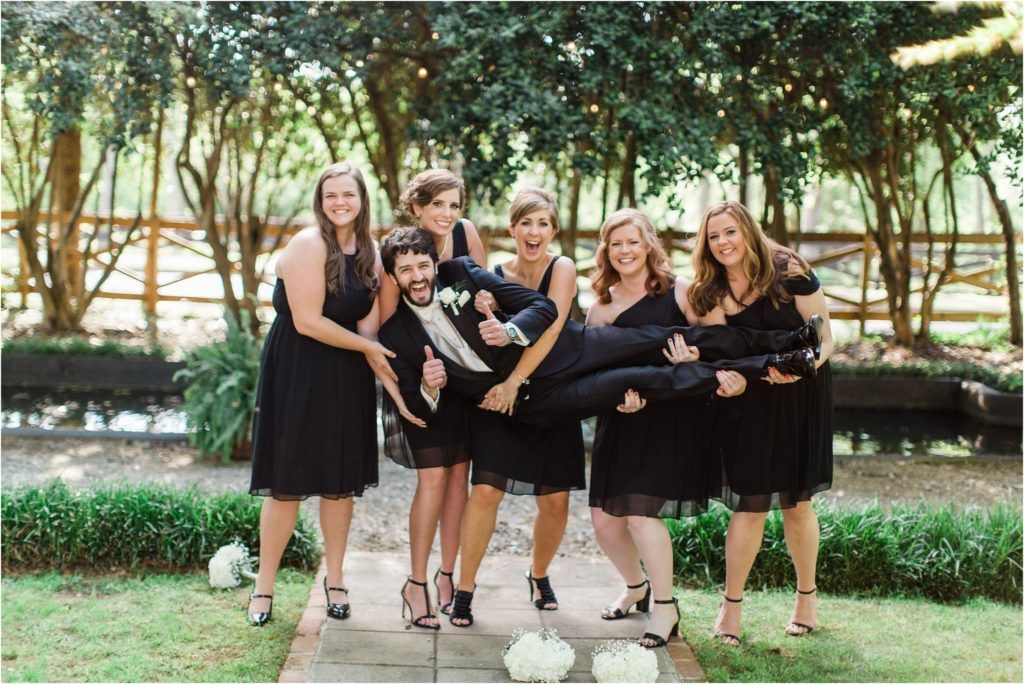 Bridesmaids in black dresses striking fun poses together on garden pathway.