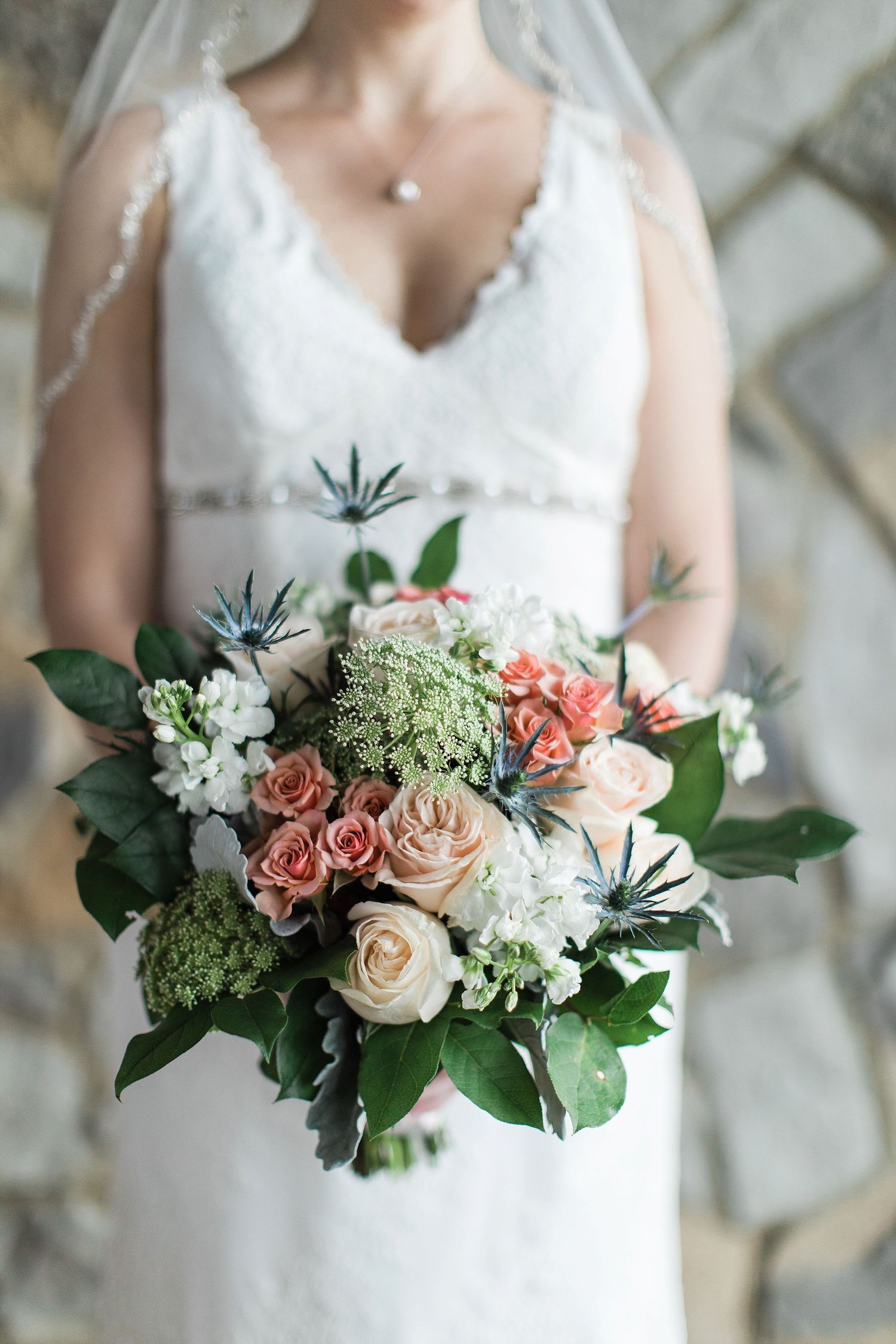 Close-up of bridal bouquet with roses, greenery and delicate florals against white dress.
