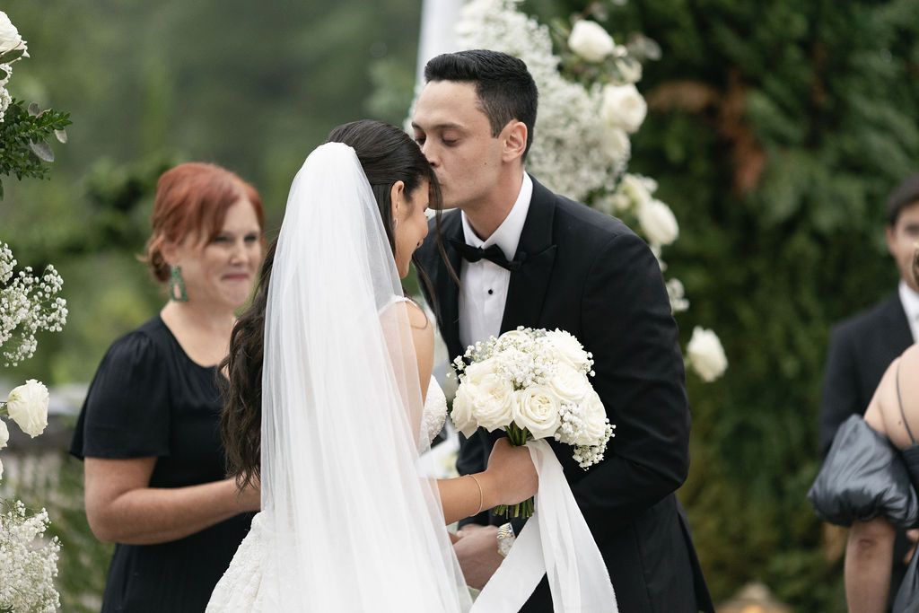 Outdoor wedding ceremony with floral decorations and white bouquet.