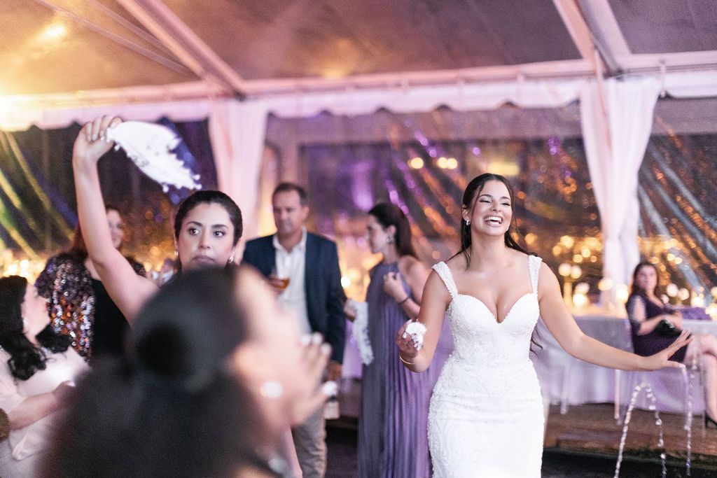 Joyful dancing and celebration under a white tent with purple lighting at a wedding reception.