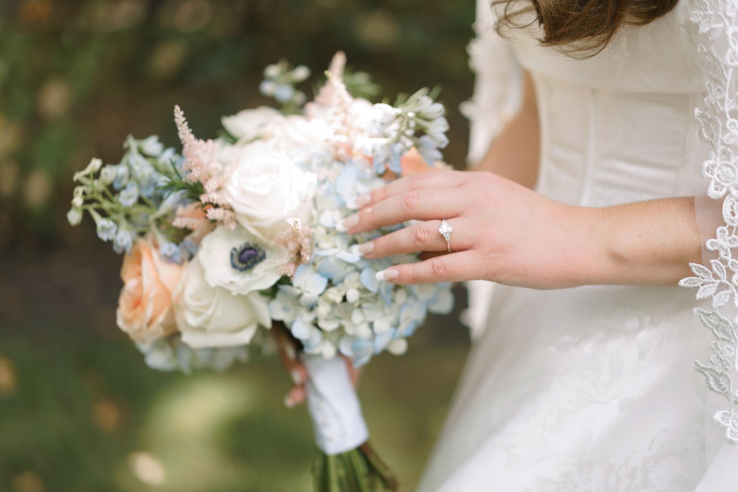 Bride holds a romantic bouquet of white roses, blue hydrangeas, and anemones on her wedding day.