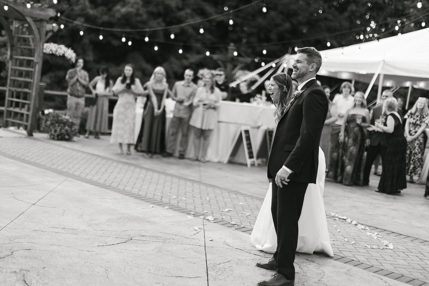 Black and white photo of wedding reception dancing under string lights.