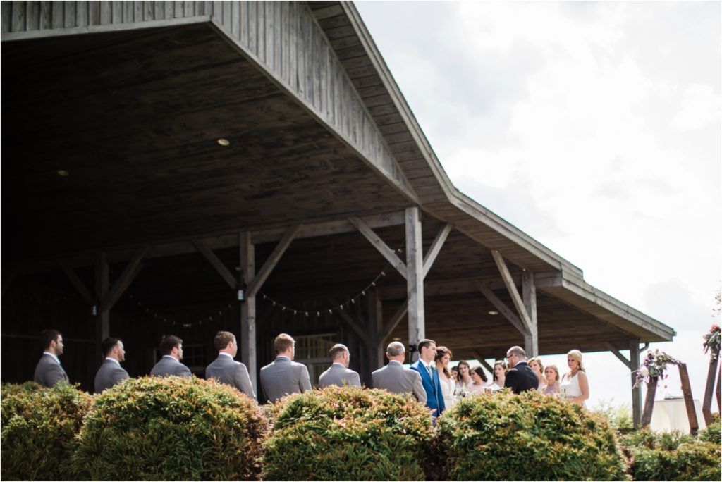 Wedding ceremony setup at rustic barn venue with guests gathered on covered porch.