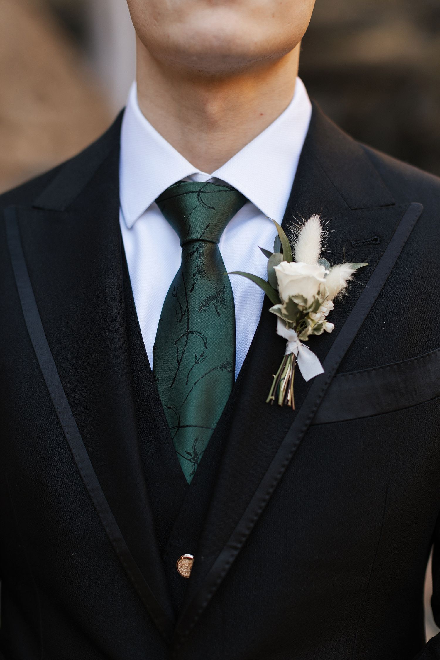 Close-up of formal black suit jacket with emerald green tie and white floral boutonniere.